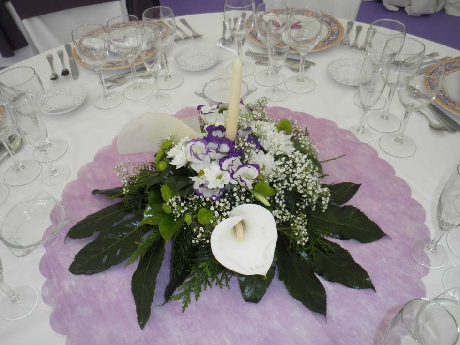 Centro de mesa floral blanco con una vela sobre una decoración de mesa redonda morada en una mesa de comedor formal.