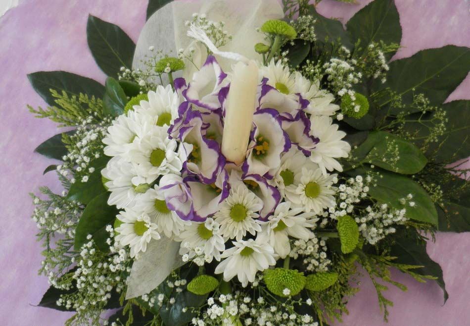 Arreglo floral blanco y morado con follaje sobre un fondo rosa.