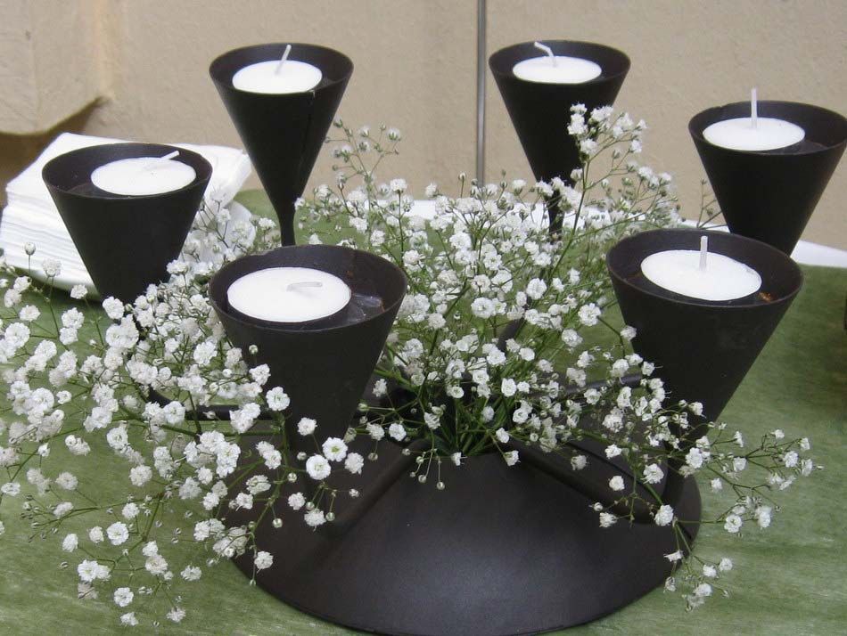 Centro de mesa con candelabro negro, velas blancas y flores de paniculata.