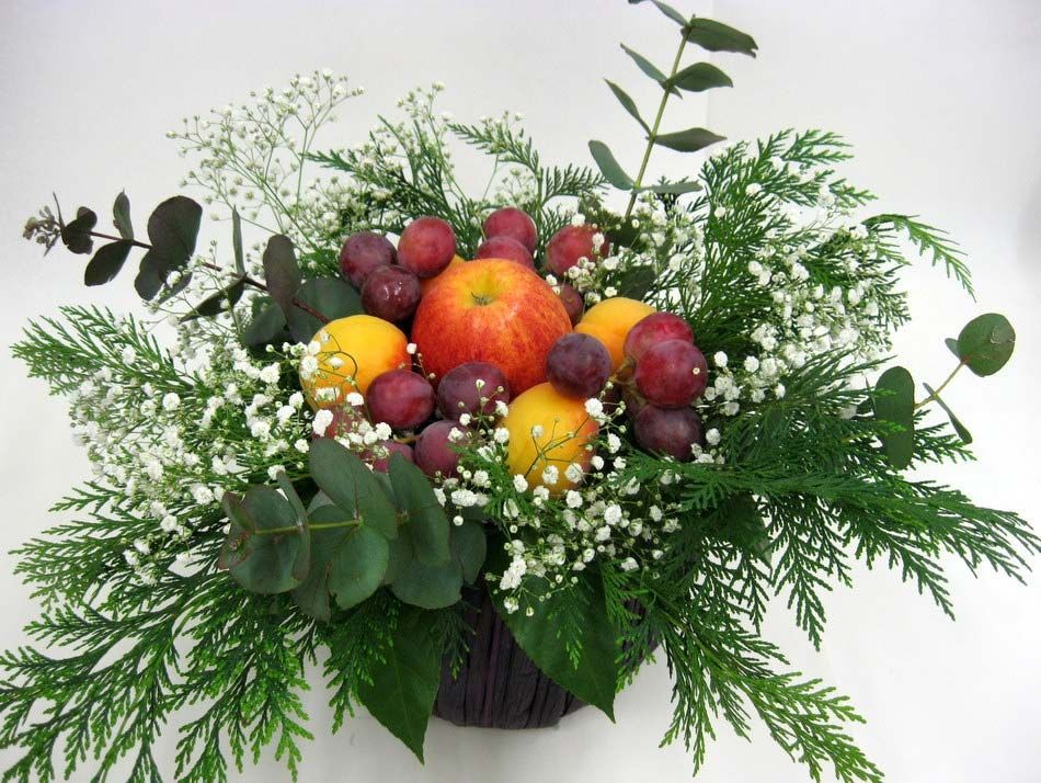 Arreglo floral con frutas y follaje, con manzanas, uvas y bayas en un jarrón.
