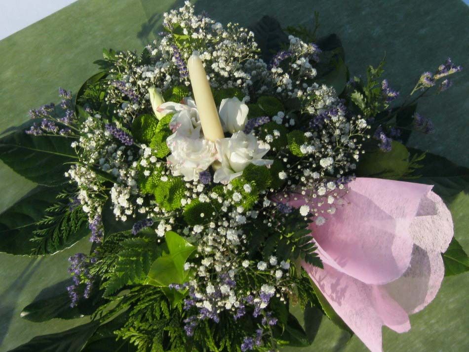 Corona floral con vela blanca y cinta rosa sobre césped.
