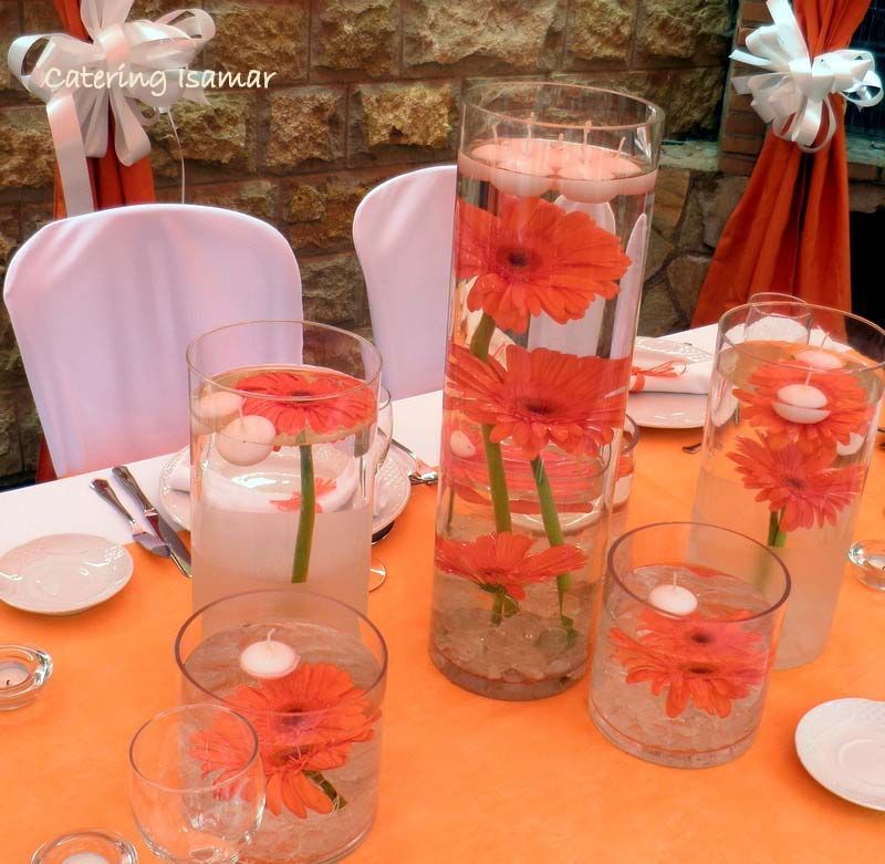 Centros de mesa florales con velas en jarrones de cristal sobre una mesa naranja en una mesa de evento decorada.
