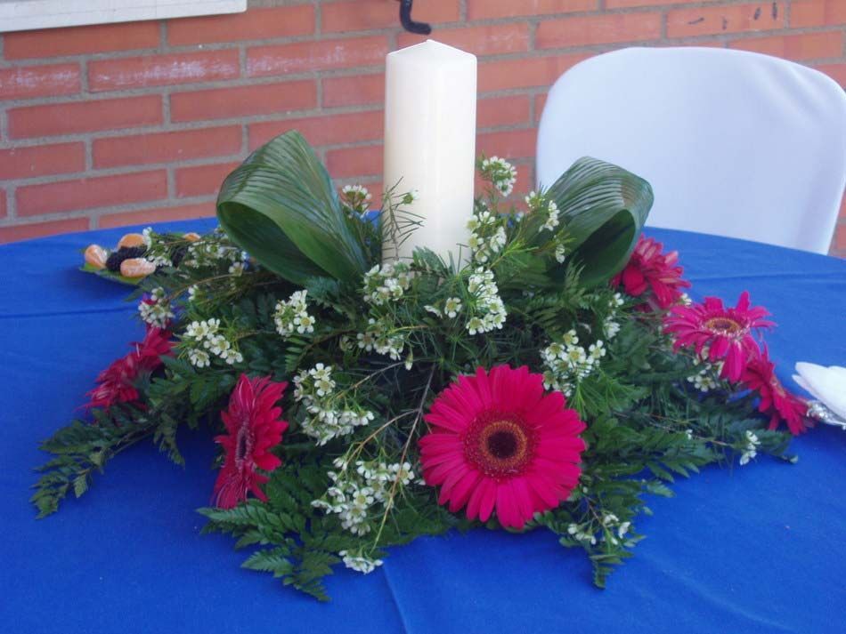Centro de mesa con velas blancas y flores rosas y blancas sobre un mantel azul.