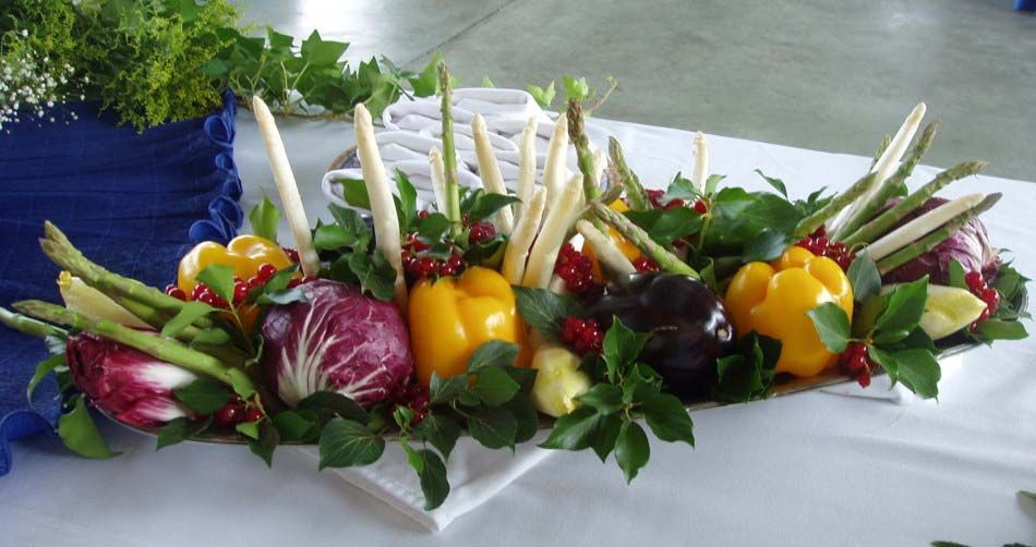 Centro de mesa colorido con verduras: pimientos, rábanos y hojas verdes sobre un mantel blanco.