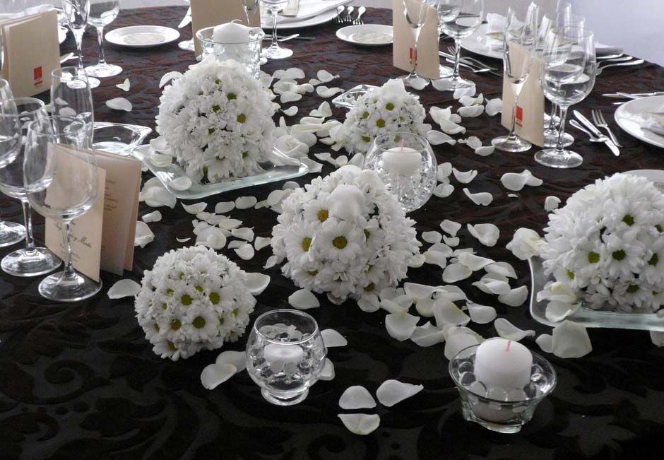 Centro de mesa negro con arreglos florales blancos, velas y pétalos esparcidos en una mesa de evento formal.