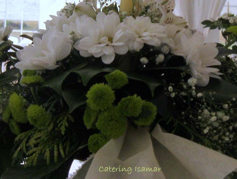 Ramo floral blanco y verde con cinta, dispuesto como centro de mesa en un evento en interiores.
