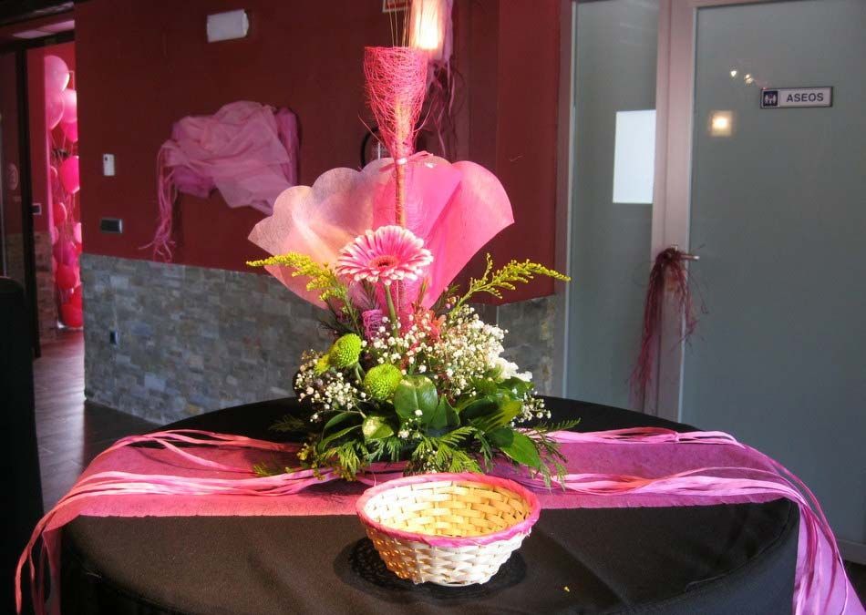 Arreglo floral con envoltorio rosa sobre una mesa en una habitación interior con poca luz.
