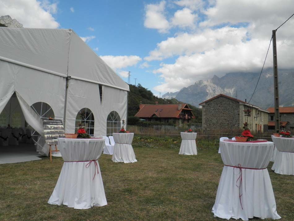 Montaje para evento al aire libre con carpa blanca, mesas de cóctel y paisaje montañoso de fondo bajo un cielo nublado.