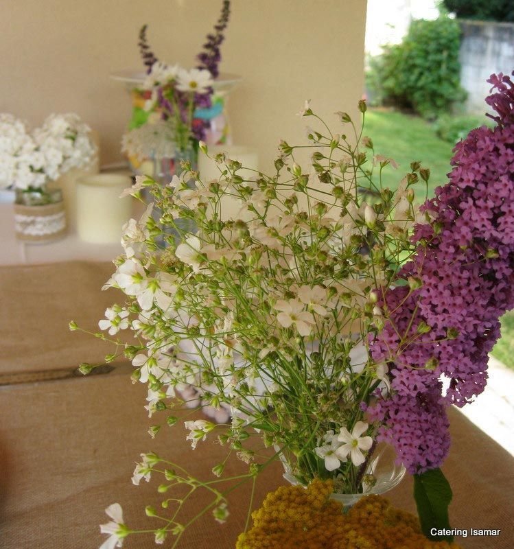 Ramo de flores silvestres blancas, moradas y amarillas sobre una mesa cerca de una vista al jardín.