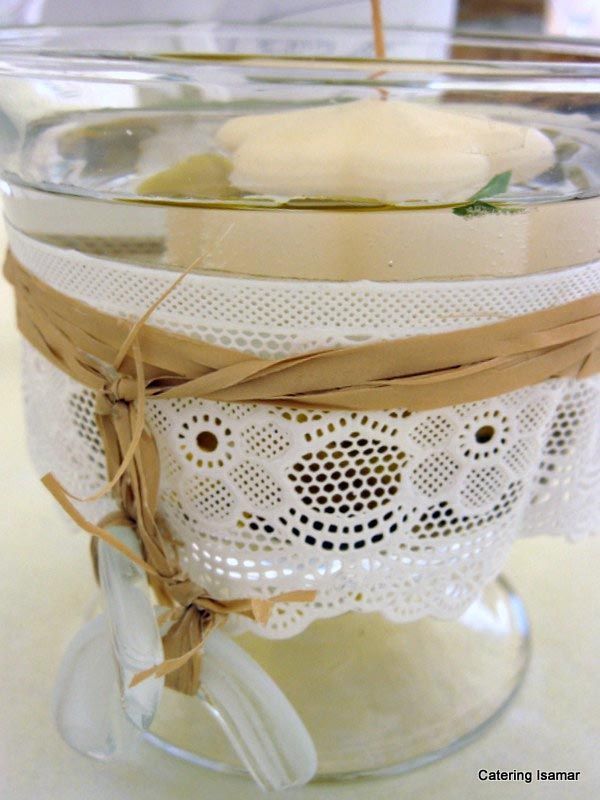 Frasco de vidrio envuelto con encaje blanco y cordel, decorado con una flor blanca.