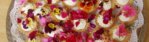 Surtido de pasteles cubiertos con crema y flores en una bandeja decorativa.