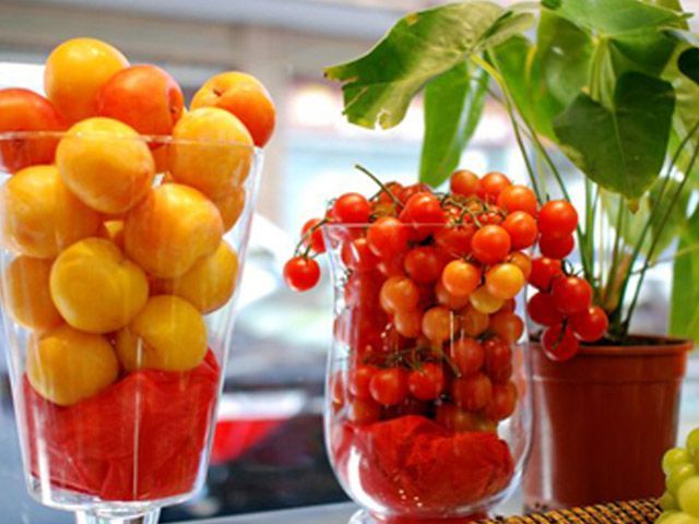 Frascos de vidrio llenos de tomates cherry rojos y amarillos apilados sobre una encimera de cocina con macetas.