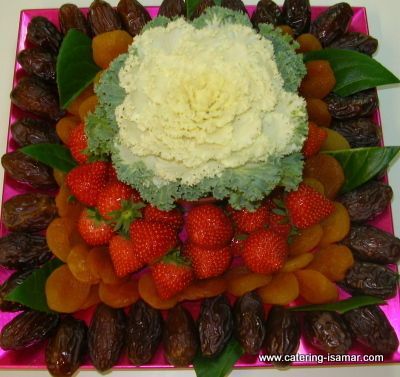 Plato de frutas con forma de flor con fresas, albaricoques, uvas y hojas verdes sobre una bandeja rosa.