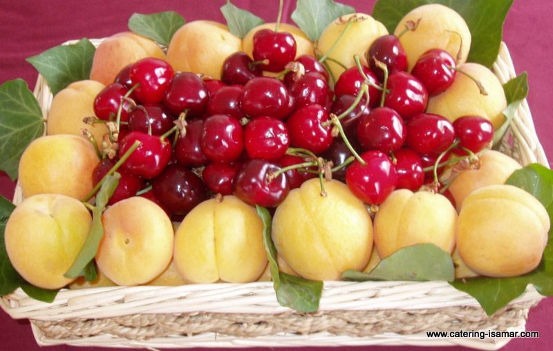 Cesta de cerezas rojas y albaricoques amarillos con hojas verdes y asa de mimbre.