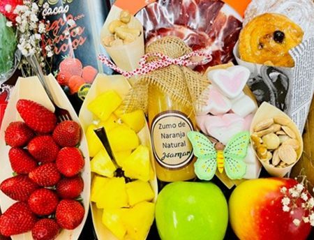 Surtido de frutas y dulces coloridos dispuestos en una cesta de regalo decorativa.