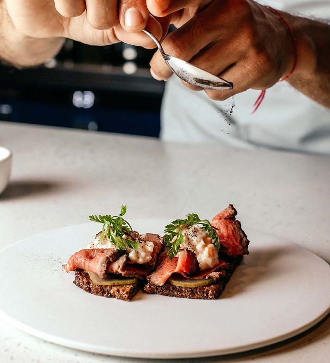 Chef decorando un aperitivo emplatado con salmón, hierbas y tostadas en un plato blanco.