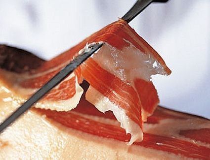 Lonchas de jamón curado cortadas con cuchillo sobre una tabla de madera