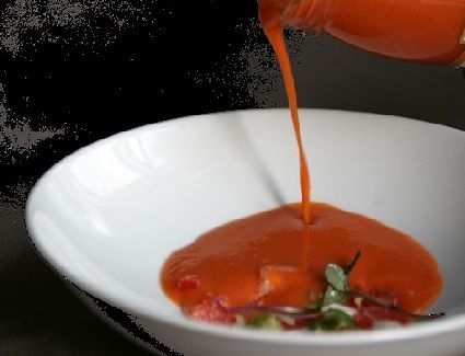 Se vierte salsa roja en un tazón blanco con algunas verduras en el fondo.