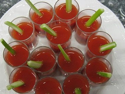 Vasos de jugo rojo con palitos de apio en una bandeja blanca.