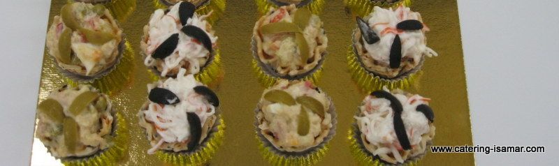 Bandeja de seis pequeños cupcakes decorados con glaseado blanco y detalles oscuros sobre un fondo blanco.