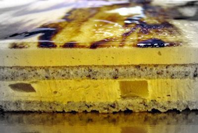 Primer plano de un postre amarillo en capas con un chorrito de chocolate por encima y una base blanca desmenuzable.