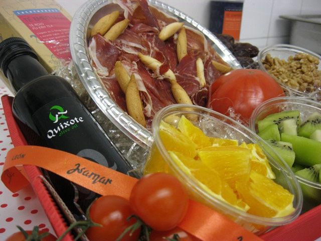 Variedad de embutidos y verduras dispuestos en una bandeja, entre ellos jamón, cítricos, tomates y kiwi.