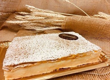 Rebanada de pastel de crema de azúcar glas sobre una bandeja de madera decorada con trigo seco.