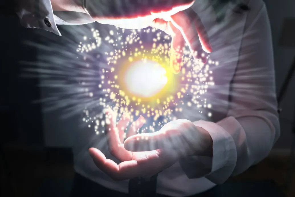 Una mano dibuja con lápiz una carta astral. Cerca se disponen símbolos del zodíaco y piedras preciosas.