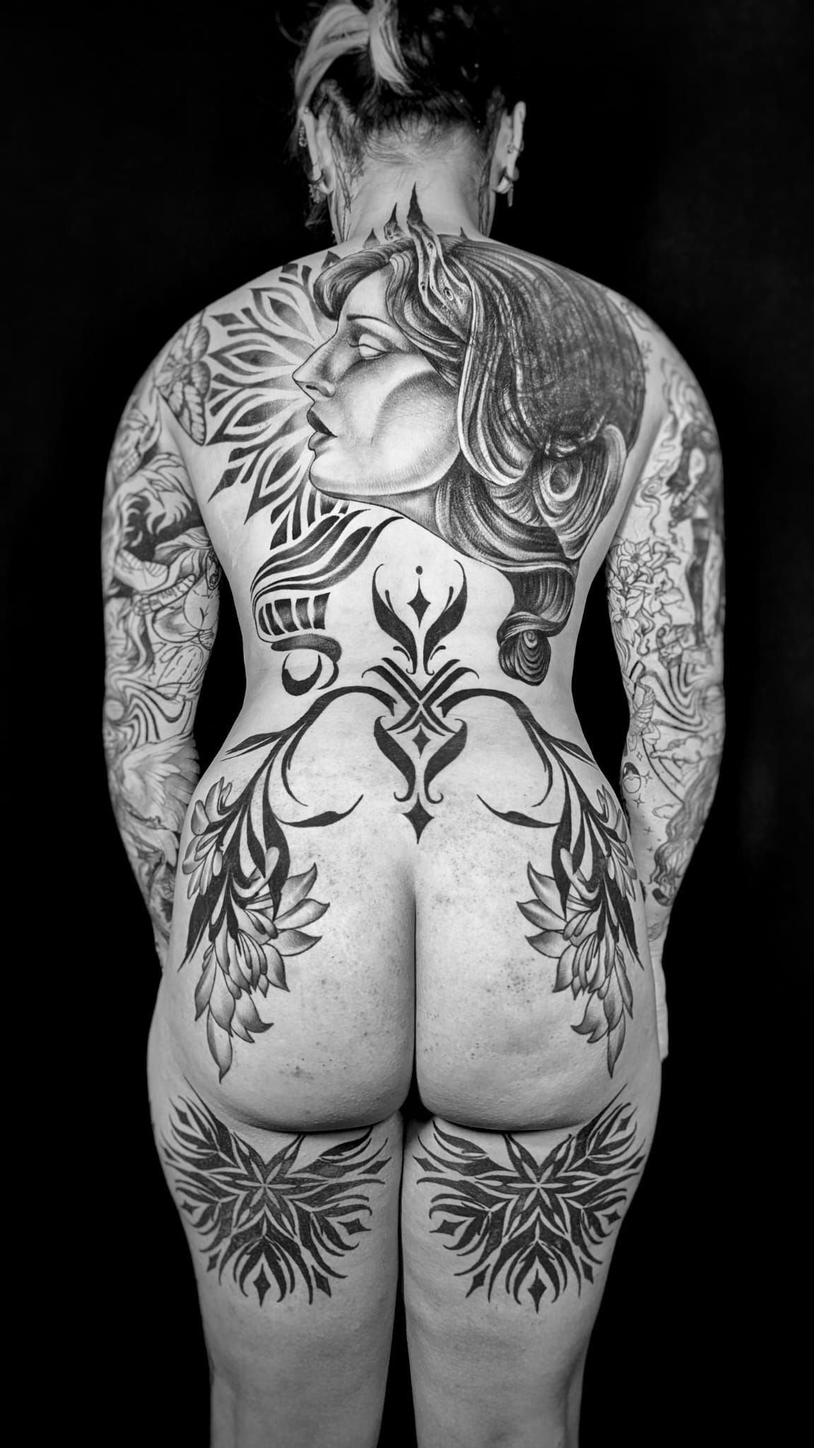Persona vista de espaldas, con extensos tatuajes de tinta negra que cubren su espalda, glúteos y parte superior de los muslos.
