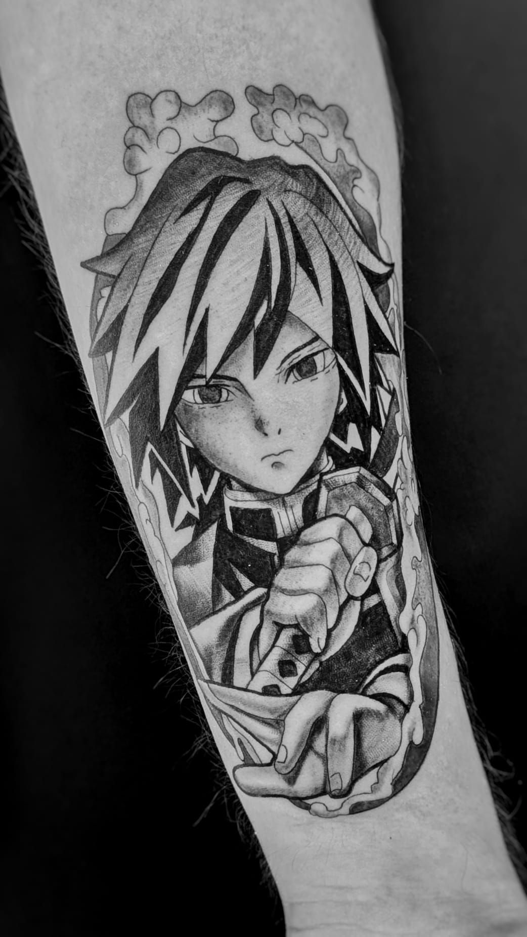Tatuaje en blanco y negro de un personaje de anime con el pelo puntiagudo, sosteniendo una espada, enmarcado por olas de agua estilizadas.