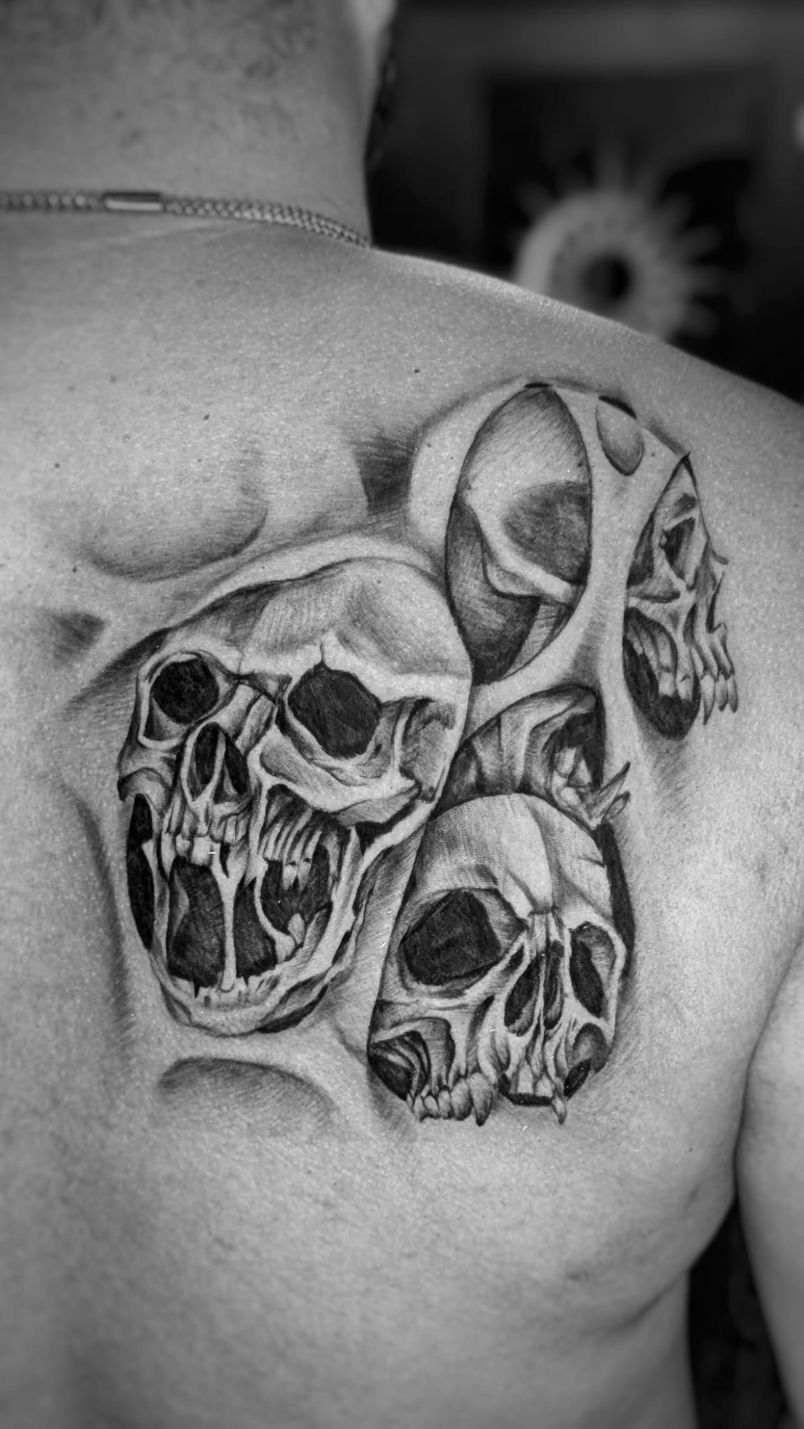 Un tatuaje en blanco y negro en el omóplato de una persona que presenta tres calaveras realistas integradas en efectos de piel desgarrada.