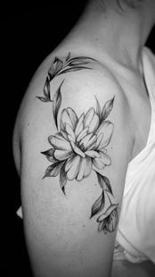Un tatuaje en blanco y negro de una gran flor con hojas y capullos, situado en la parte superior del brazo.