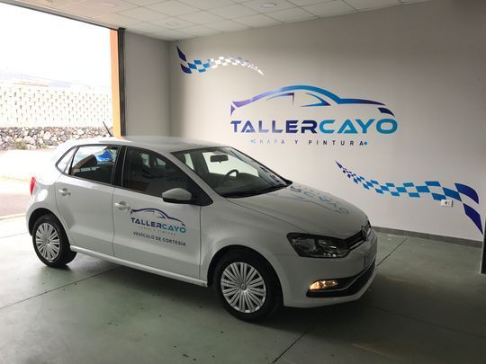 Un coche blanco está aparcado delante de una pared que dice tallercayo
