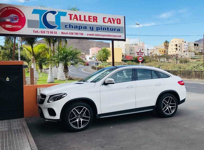 Un coche blanco está aparcado delante de un cartel que dice taller cayo