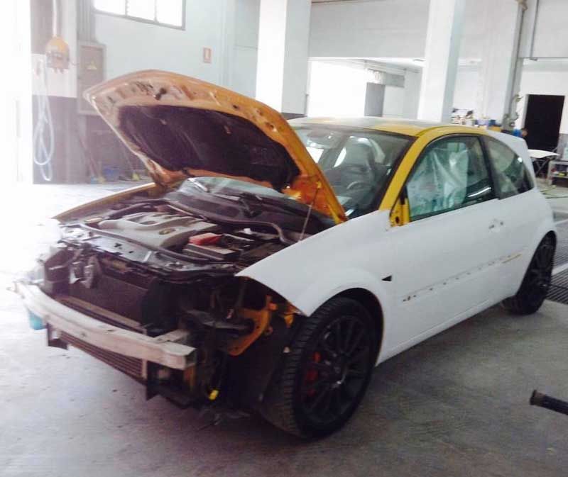 Un coche blanco con el capó abierto en un garaje.