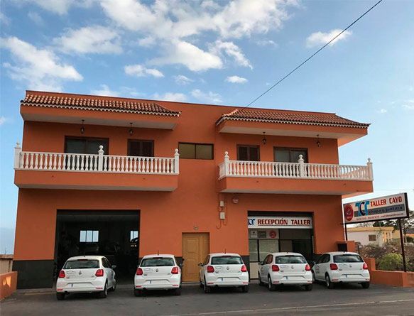 Una fila de coches están aparcados delante de un edificio naranja.