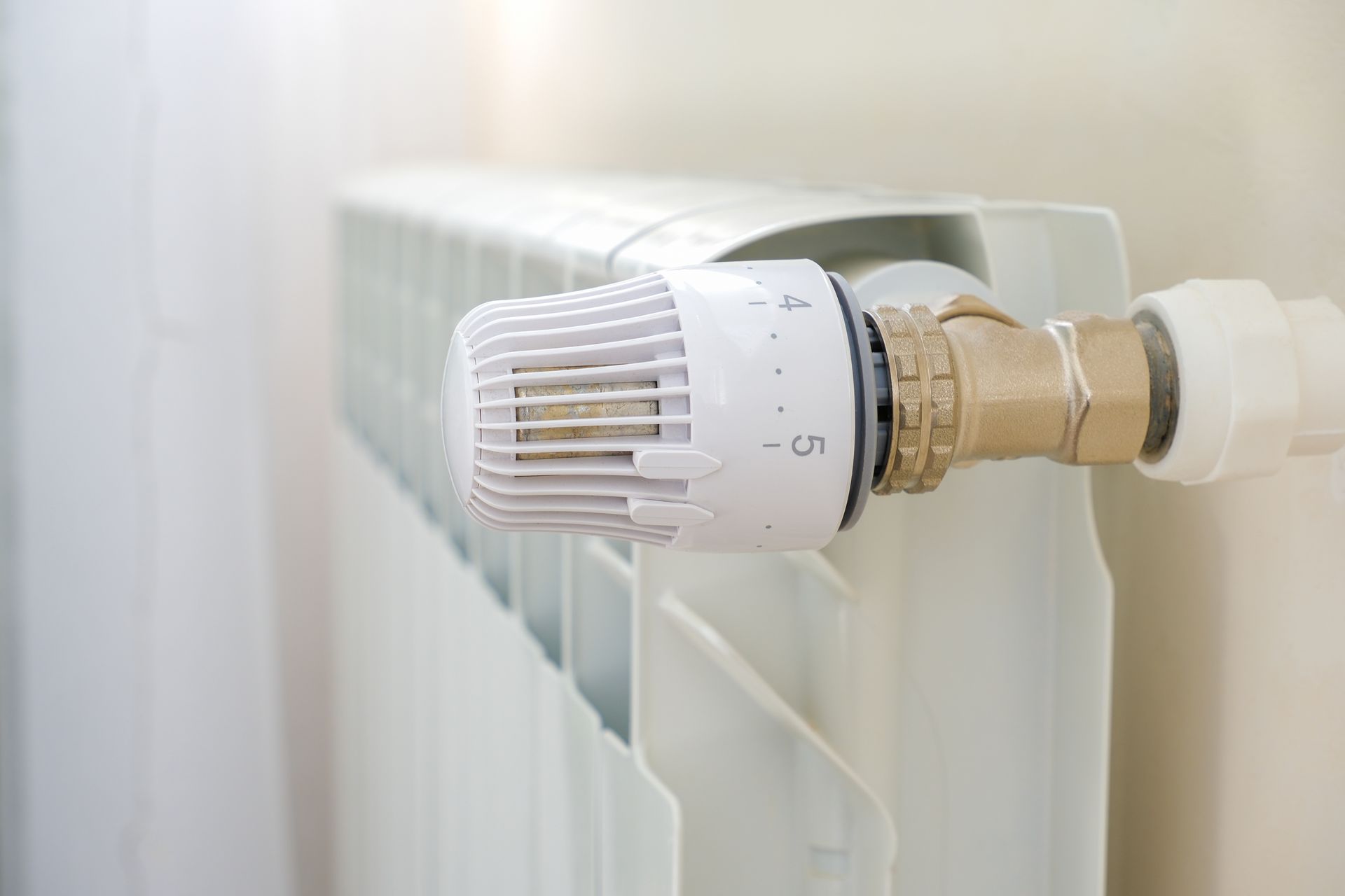 Gros plan sur une tête thermostatique blanche montée sur un radiateur dans une pièce lumineuse.