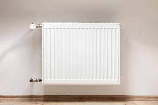 Radiateur blanc fixé au mur sur un mur beige au-dessus d’un plancher en bois.