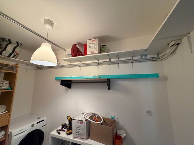 Buanderie avec des étagères, des tringles, une suspension et un lave-linge à côté de boîtes de rangement avec des câbles sous l'étagère.