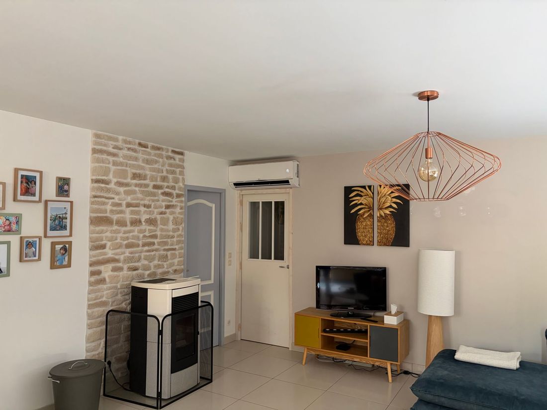 Salon moderne avec mur d’accent en pierre, télévision, lampe suspendue, climatiseur et photos encadrées.