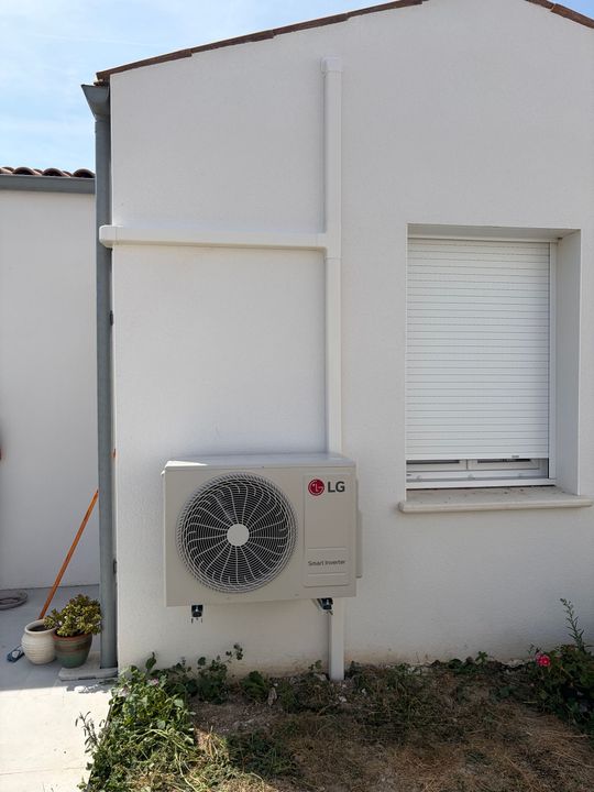 Mur extérieur avec un climatiseur fixé au mur, une petite fenêtre et une plante en pot près d’un bâtiment.