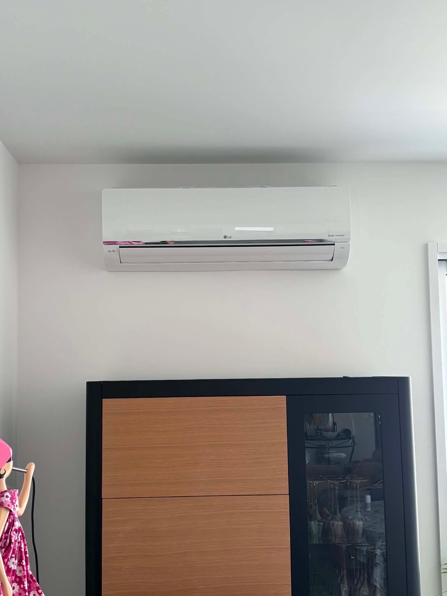 Climatiseur mural au-dessus d’une armoire noire dans une pièce blanche.