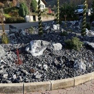 Kreisverkehr mit dunklem Kies, grossen Steinen und spiralförmigen Formgehölzen.