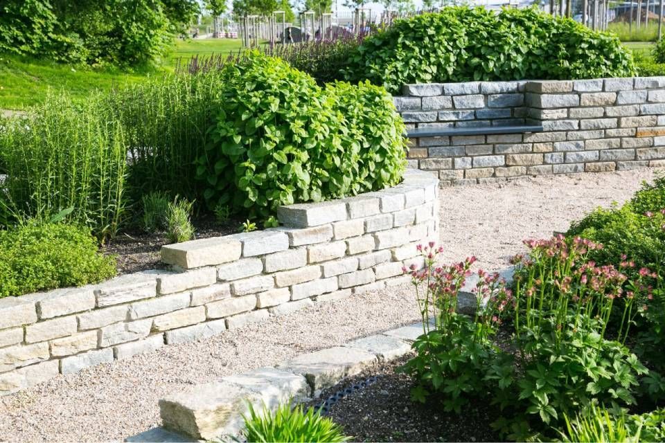 Steinmauern mit üppiger Bepflanzung in einer Gartenanlage. Ein Kiesweg führt nach oben.