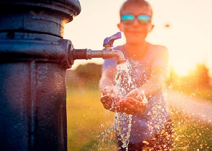 Un niño pequeño se vierte agua de un grifo en las manos.
