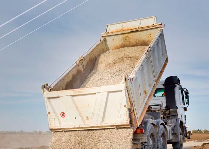 Un camión de volteo circula por un camino de tierra.