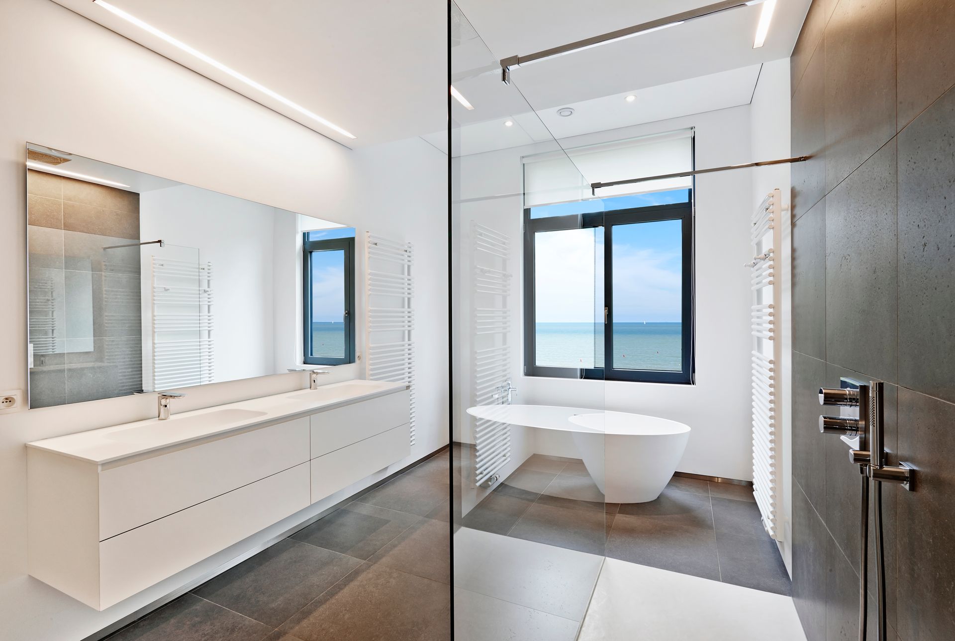 Modernes Badezimmer mit Doppelwaschbecken, freistehender Badewanne und großem Fenster mit Blick auf das Wasser