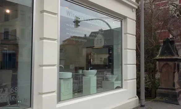 Schaufenster mit hellgrünen Ausstellungsstücken und einer Hängelampe im Inneren