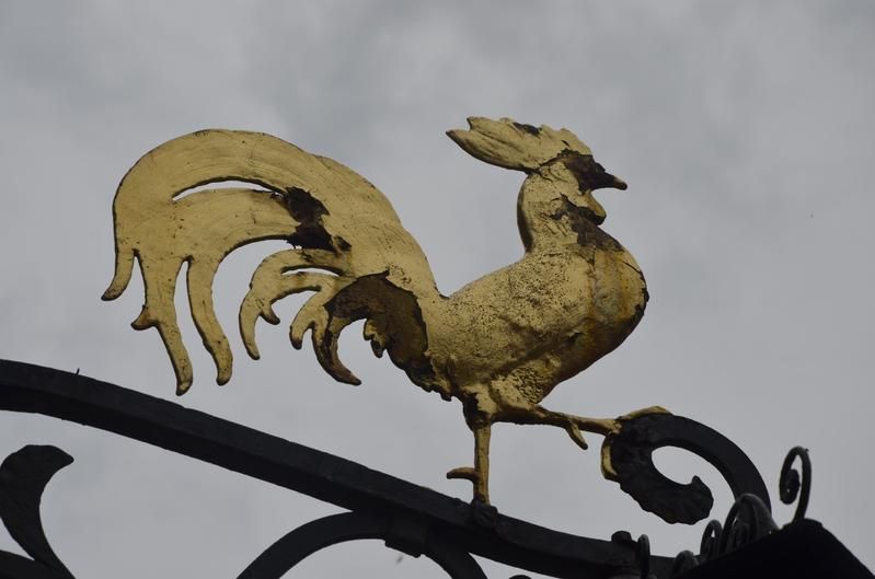 Ein goldener Hahn sitzt auf einem schmiedeeisernen Geländer