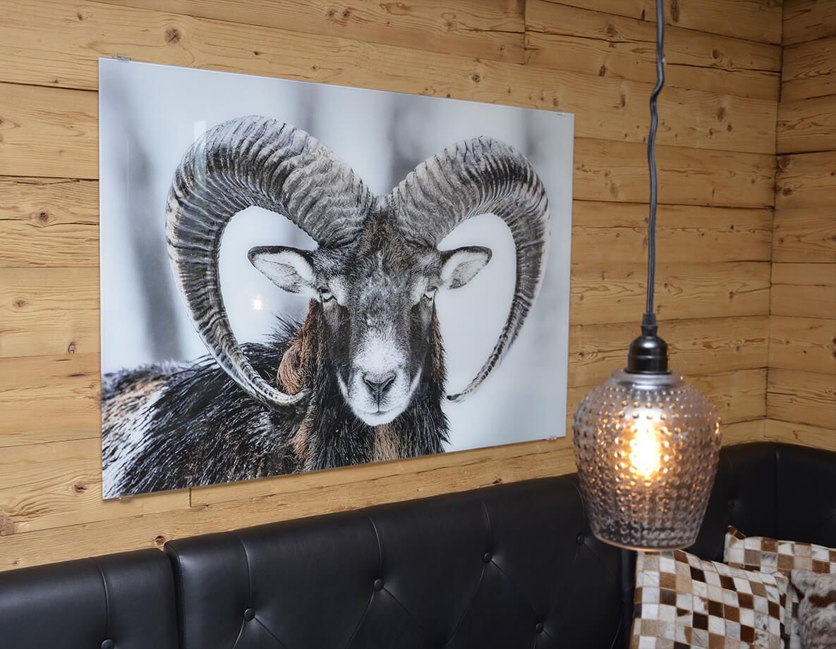 An einer Holzwand hängt ein Bild einer Ziege mit Hörnern.
